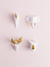 4 assorted white and gold animal head magnets on a light pink background
